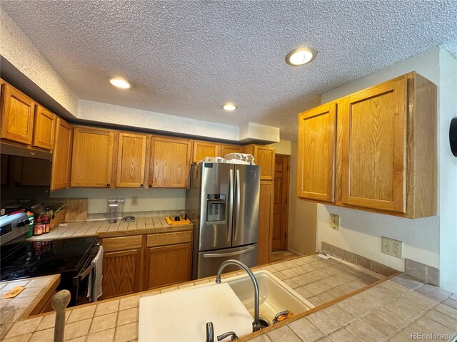 971 S Evanston Cir, Aurora, CO 80012 - kitchen with appliances with stainless steel finishes, tile counters, a textured ceiling, a sink, and tile patterned flooring