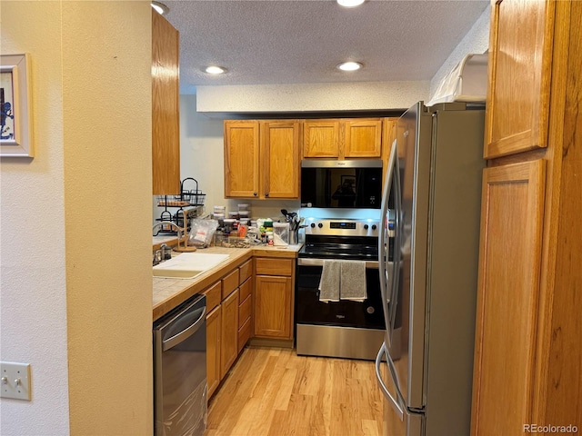 971 S Evanston Cir, Aurora, CO 80012 - kitchen with stainless steel appliances, tile countertops, light wood-type flooring, brown cabinetry, and a textured ceiling