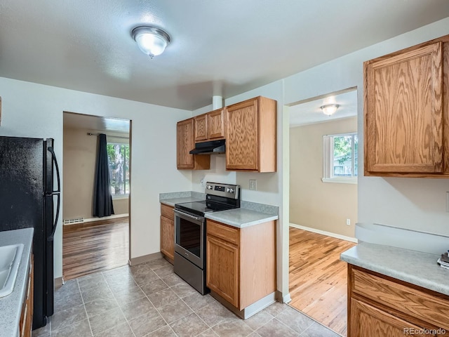 1455 S Zephyr St, Lakewood, CO 80232 - kitchen with stainless steel electric stove, under cabinet range hood, light countertops, freestanding refrigerator, and brown cabinets