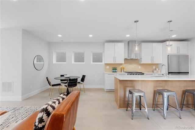 3725 N Franklin St, Denver, CO 80205 - kitchen featuring visible vents, a sink, a kitchen breakfast bar, stainless steel fridge, and wall chimney range hood