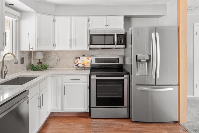 6353 W 78th Ave, Arvada, CO 80003 - kitchen with appliances with stainless steel finishes, white cabinetry, light stone counters, decorative backsplash, and light wood-style floors