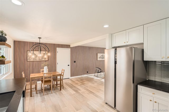 kitchen with dark countertops, light wood-type flooring, white cabinets, freestanding refrigerator, and a notable chandelier