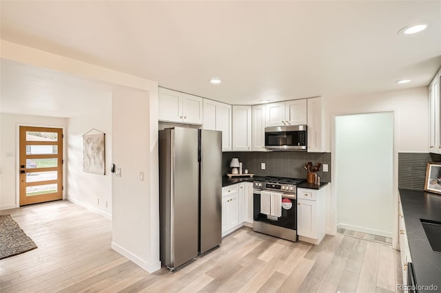 kitchen with white cabinets, dark countertops, light wood-style flooring, stainless steel appliances, and backsplash
