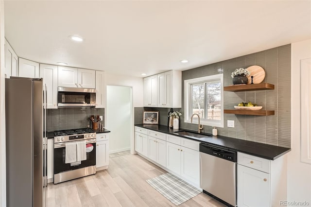 kitchen with decorative backsplash, dark countertops, white cabinetry, a sink, and appliances with stainless steel finishes