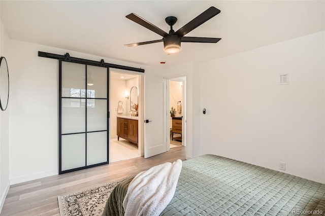 bedroom with connected bathroom, a ceiling fan, a barn door, and light wood-style flooring
