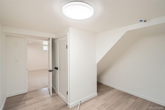 additional living space featuring baseboards, a textured ceiling, and light wood-style flooring