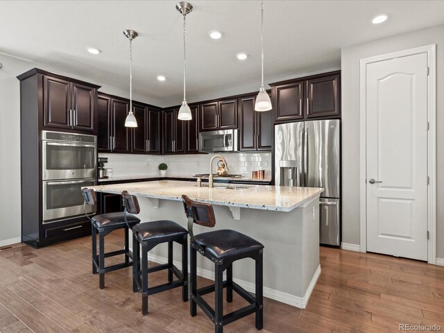 5439 Verbena St, Denver, CO 80238 - kitchen featuring stainless steel appliances, wood finished floors, light stone countertops, backsplash, and decorative light fixtures