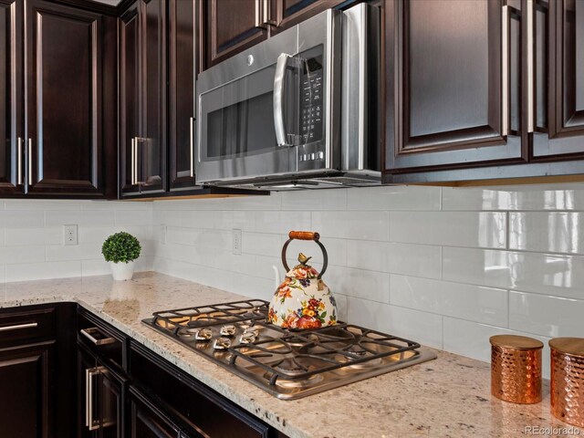 5439 Verbena St, Denver, CO 80238 - kitchen featuring stainless steel appliances, decorative backsplash, dark brown cabinetry, and light stone counters