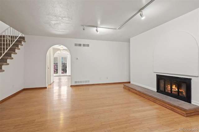 unfurnished living room featuring rail lighting, light hardwood / wood-style floors, and a textured ceiling