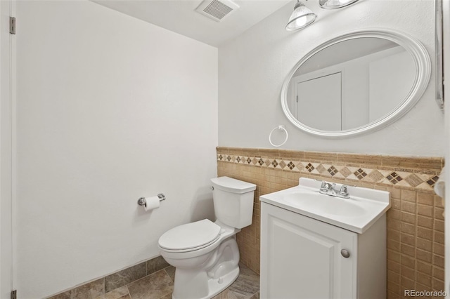 bathroom with vanity, toilet, and tile walls