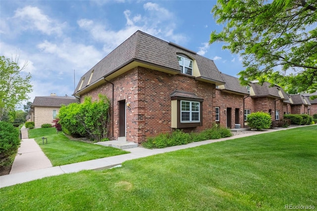 view of front of house with brick siding, mansard roof, a shingled roof, and a front lawn