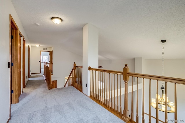 hall featuring a textured ceiling, carpet floors, and an upstairs landing