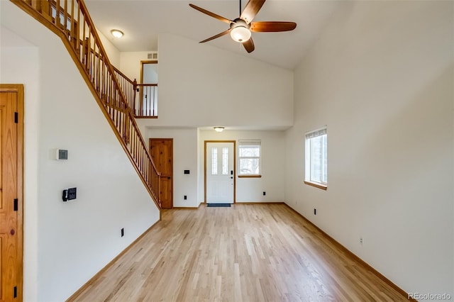 unfurnished living room featuring a high ceiling, stairway, a ceiling fan, and light wood-style floors