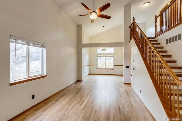 unfurnished living room featuring visible vents, stairway, light wood-style floors, high vaulted ceiling, and ceiling fan with notable chandelier