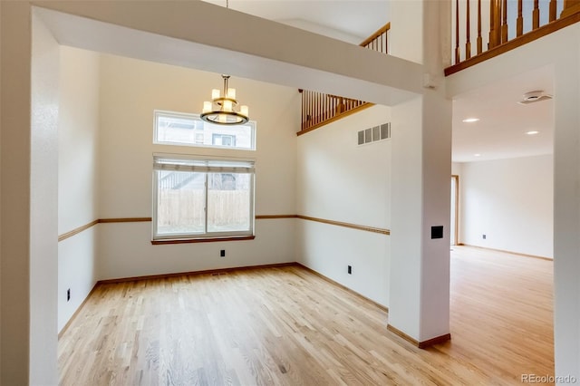 spare room with baseboards, visible vents, a towering ceiling, wood finished floors, and an inviting chandelier