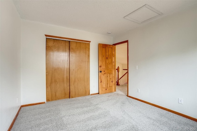 unfurnished bedroom with attic access, carpet, a closet, and baseboards