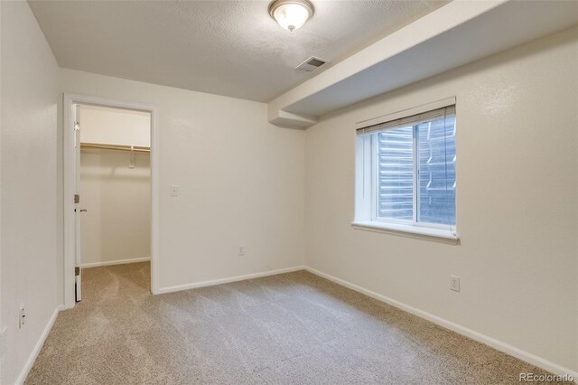 unfurnished bedroom featuring a textured ceiling, visible vents, baseboards, carpet, and a walk in closet