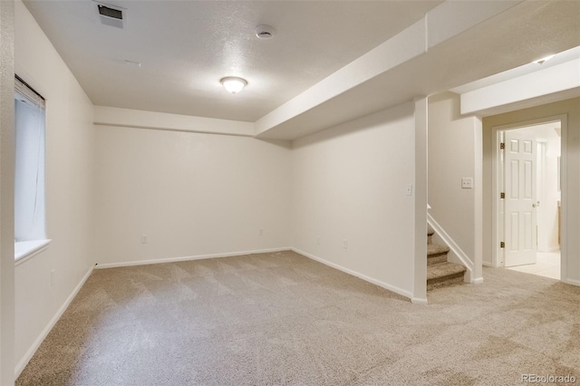 finished basement featuring light colored carpet, visible vents, baseboards, and stairs