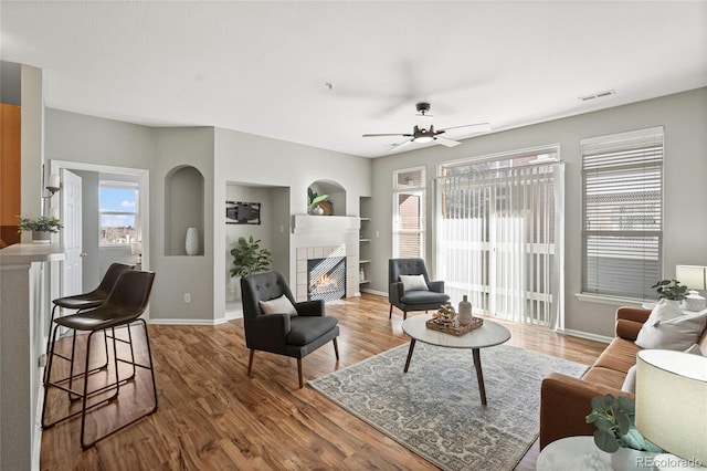 living room with built in shelves, ceiling fan, a fireplace, and hardwood / wood-style floors