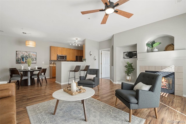 living room featuring a tile fireplace, dark wood-type flooring, and ceiling fan