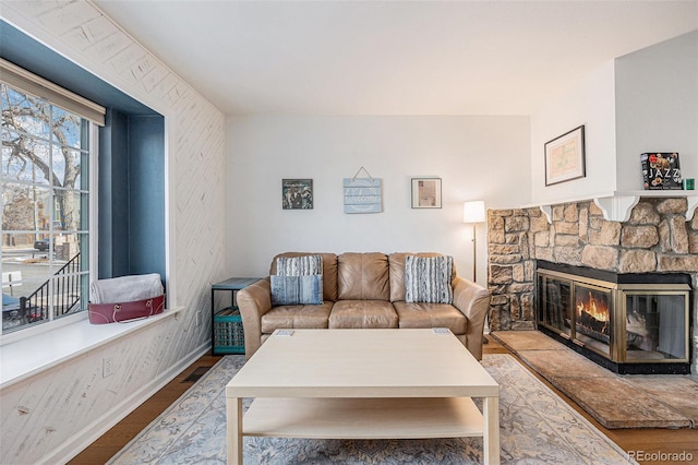 living room featuring a stone fireplace, wood finished floors, and baseboards