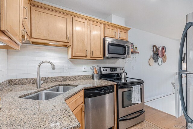 kitchen featuring tasteful backsplash, appliances with stainless steel finishes, light stone counters, and a sink