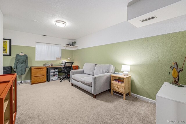office featuring visible vents, light carpet, baseboards, and a textured wall
