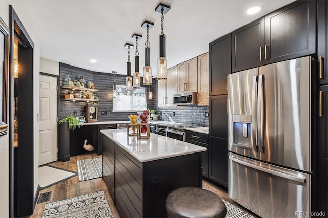 kitchen with appliances with stainless steel finishes, hanging light fixtures, decorative backsplash, a center island, and light wood-type flooring