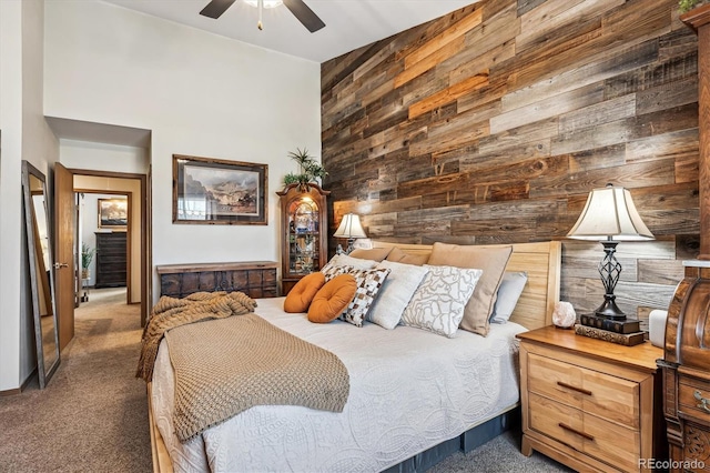 bedroom featuring ceiling fan, carpet, wood walls, and a towering ceiling