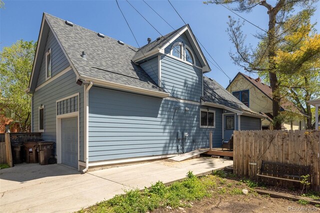 rear view of property featuring fence, an attached garage, a shingled roof, and concrete driveway