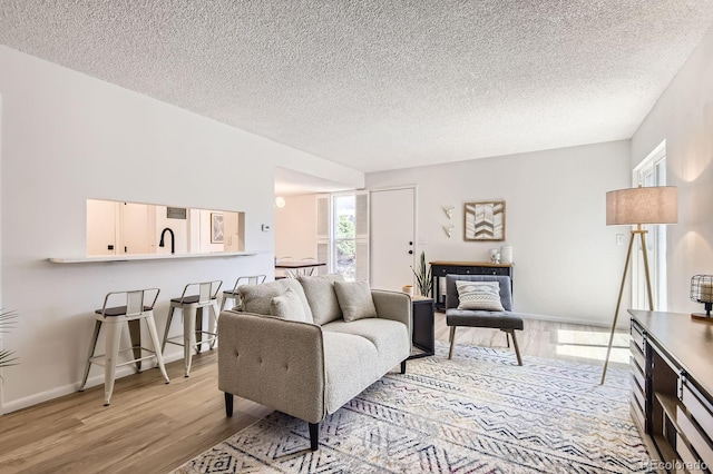 living room featuring light wood-type flooring, a textured ceiling, and baseboards