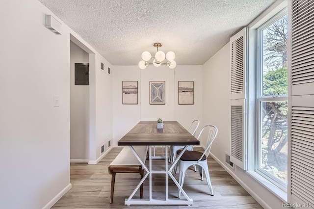 dining room featuring healthy amount of natural light, light wood finished floors, a textured ceiling, a chandelier, and electric panel