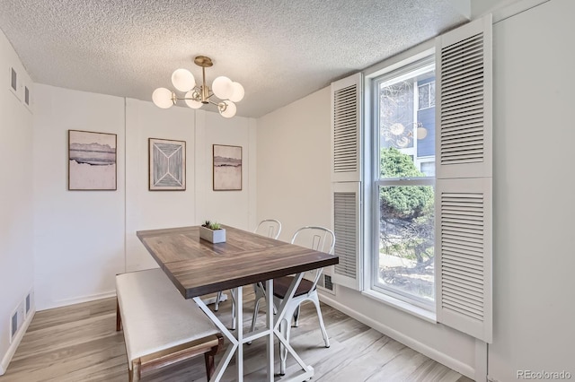 dining area featuring a chandelier, a textured ceiling, light wood finished floors, and baseboards