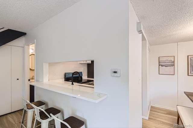 kitchen with a textured ceiling, a kitchen breakfast bar, light wood-style floors, and light countertops