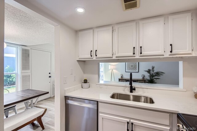 kitchen with stainless steel dishwasher, a sink, range with electric stovetop, light countertops, and white cabinets