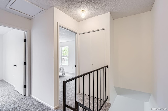 hall featuring carpet floors, a textured ceiling, baseboards, and an upstairs landing
