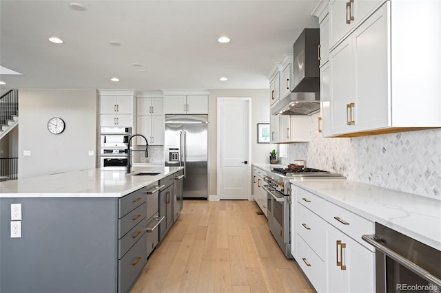 kitchen featuring high end appliances, wall chimney exhaust hood, white cabinetry, and light hardwood / wood-style flooring