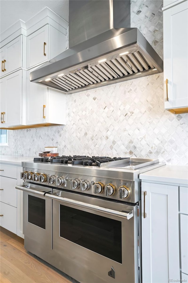 kitchen featuring wall chimney exhaust hood, light hardwood / wood-style flooring, range with two ovens, backsplash, and white cabinets