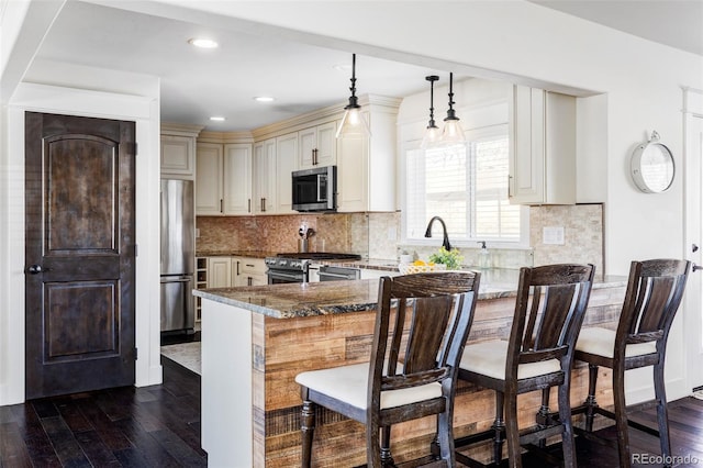 kitchen featuring stainless steel appliances, hanging light fixtures, kitchen peninsula, dark stone countertops, and a breakfast bar area