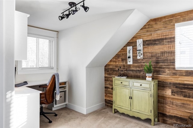 office space featuring wood walls, light colored carpet, lofted ceiling, and built in desk