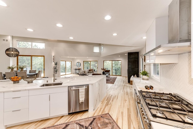 kitchen featuring wall chimney range hood, stainless steel dishwasher, cooktop, and light stone countertops