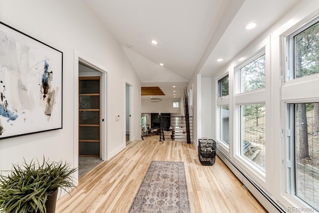 corridor with a baseboard heating unit, hardwood / wood-style floors, and high vaulted ceiling