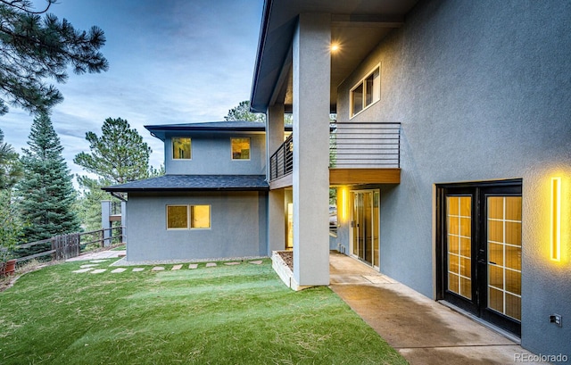 rear view of property with french doors, a balcony, a patio area, and a lawn