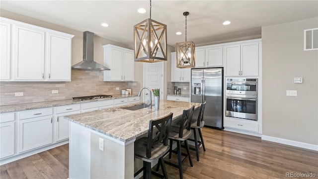 kitchen featuring a sink, decorative backsplash, wood finished floors, wall chimney range hood, and appliances with stainless steel finishes