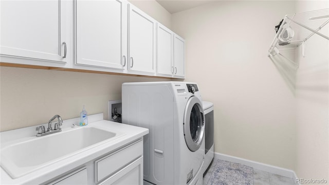 laundry area with baseboards, separate washer and dryer, cabinet space, and a sink