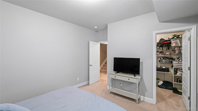 bedroom with baseboards, a closet, light colored carpet, and a walk in closet