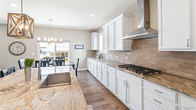kitchen featuring stainless steel gas stovetop, a sink, white cabinetry, decorative backsplash, and wall chimney range hood