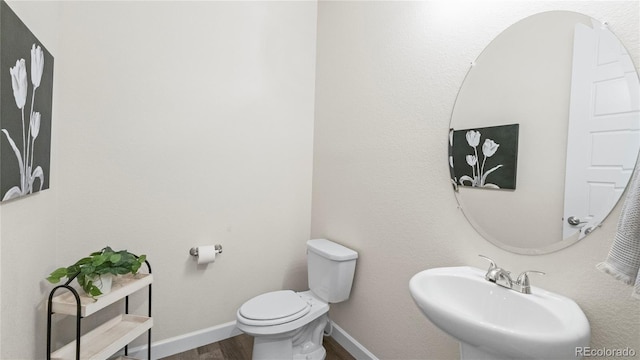 half bathroom with a sink, toilet, baseboards, and wood finished floors