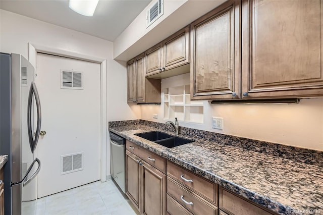 kitchen with a sink, stainless steel appliances, visible vents, and dark stone counters