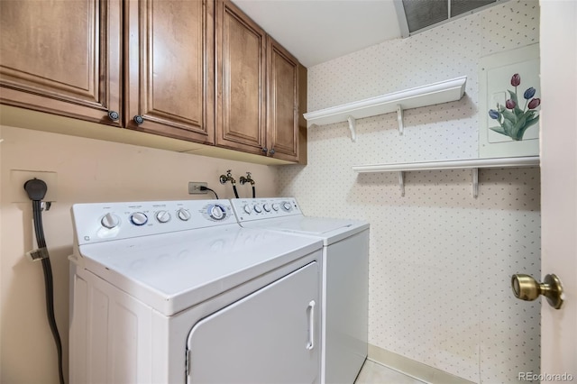 clothes washing area with washer and clothes dryer, cabinet space, and wallpapered walls